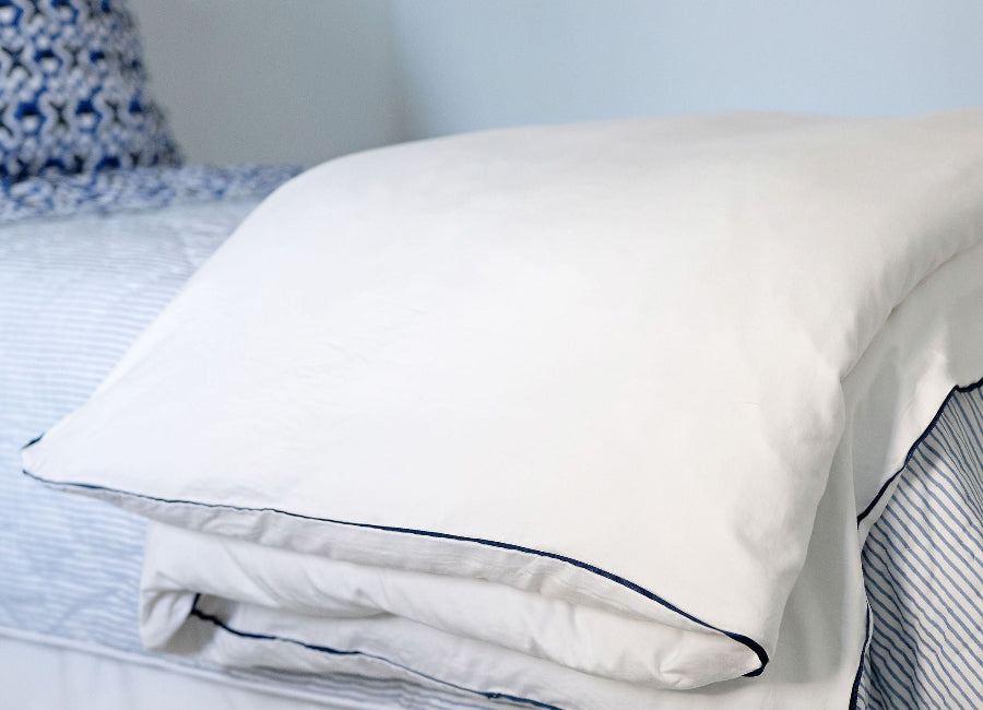 White pillow on a bed with blue trim in a bedroom setting