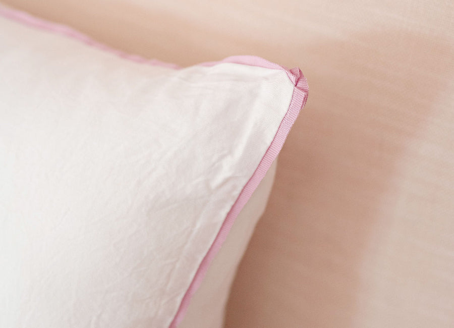 Close-up of a white pillow with pink trim on a light beige background