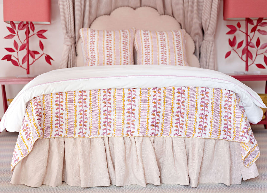 Bed with patterned bedding and pillows in a room with pink walls and decorative elements.