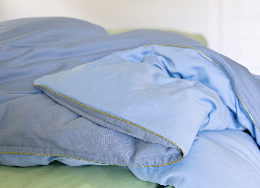 Light blue and green bedding on a bed with a white background