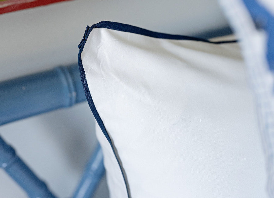 Close-up of a white pillow with blue piping on a blurred background