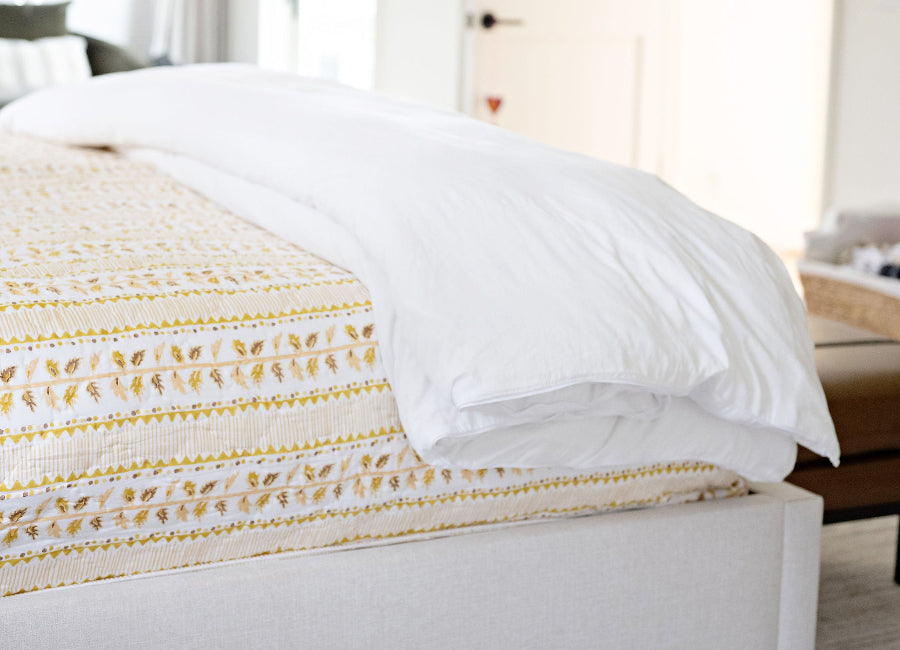 Bedroom with a bed featuring white bedding and a yellow textured blanket.