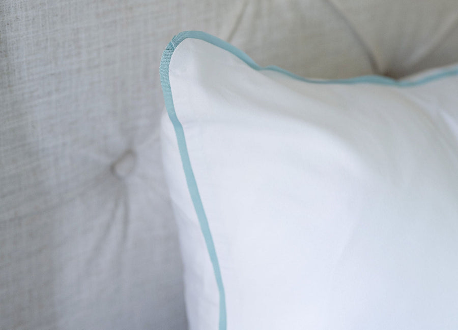 White pillow with a light blue trim on a tufted headboard